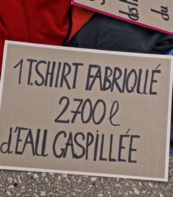 Une pancarte sur laquelle il est écrit : « un T-shirt fabriqué 2 700 litres d'eau gaspillée »